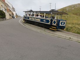 A tram with passengers on a track beside a road and hillside at Maesdu Cottage in Llandudno