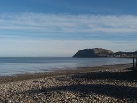 A rocky beach with calm sea water and hills in the distance at Maesdu Cottage in Llandudno
