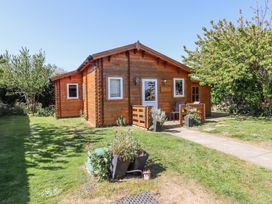 A wooden cabin with white framed windows and a small porch in a grassy garden with trees at Aurora Skies in Cresswell near Morpeth