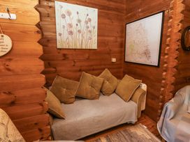 A wooden room with a sofa covered by a throw and cushions a floral painting and a framed map on the walls at Aurora Skies in Cresswell near Morpeth