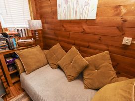 A small corner seating area with brown cushions next to a wooden shelf with books and a lamp at Aurora Skies in Cresswell near Morpeth