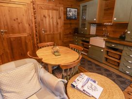 A kitchen with a wooden round table surrounded by four chairs a gray armchair with a cushion and throw a wicker table with books and a guest book on it green cabinets with a farmhouse sink and wood panel walls at Aurora Skies in Cresswell near Morpeth