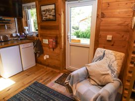 A wooden kitchen corner with a white dishwasher, fridge, kettle, armchair with cushions and a door leading outside at Aurora Skies in Cresswell near Morpeth