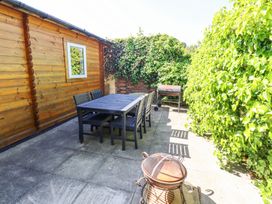 An outdoor patio with a black dining table and six chairs near a wooden shed and green leafy plants at Aurora Skies in Cresswell near Morpeth