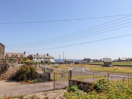 A street view with houses and a metal gate with a grassy area and sea in the background at Aurora Skies in Cresswell near Morpeth