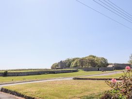 A grassy open area with a road and stone walls with trees and a stone building in the background at Aurora Skies in Cresswell near Morpeth