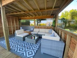 A covered outdoor seating area with wicker furniture cushions and a patterned rug at Hearthstone East Cottage in Brixham