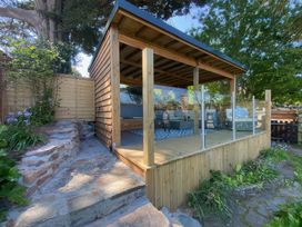 An outdoor wooden gazebo with glass paneling next to stone steps and garden at Hearthstone East Cottage in Brixham