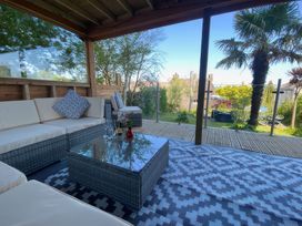 A covered outdoor seating area with cushioned chairs a glass table and a patterned rug overlooking a garden with a palm tree at Hearthstone East Cottage in Brixham