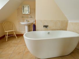 A bathroom with a bathtub, sink, and chair at Mallows Byre in Yetminster
