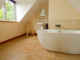 A bathroom with a bathtub, sink, mirror and chair at Mallows Byre in Yetminster