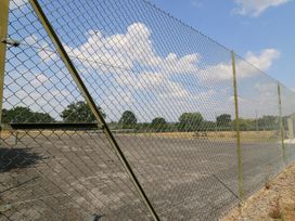 A chain link fence surrounding an open area with trees at The Cider Press, Motcombe