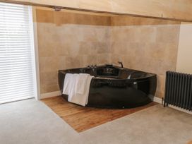 A black corner bathtub with white towels hanging on it against tiled walls on a wooden platform next to a window with blinds at Winnie's Stable Goodmanham Wold near Market Weighton