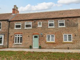 Exterior view of a brick house with multiple white framed windows and a green door with two small potted plants at The Groom's Cottage in Goodmanham Wold near Market Weighton