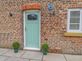 A green door set in a brick wall with two potted plants on either side and a window with blinds to the right at The Groom's Cottage Goodmanham Wold near Market Weighton