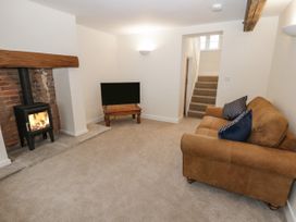 A living room with a fireplace, brown sofa, television on a wooden table, and carpeted stairs at The Groom's Cottage in Goodmanham Wold near Market Weighton