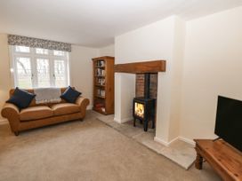 A living room with a brown sofa and blue cushions a wood burning stove a wooden bookshelf and a television on a wooden stand at The Groom's Cottage in Goodmanham Wold near Market Weighton