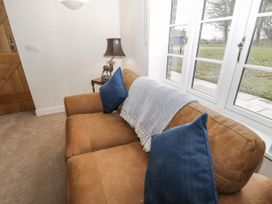 A room with a brown sofa with blue cushions and a throw blanket near a window and a wooden door at The Groom's Cottage Goodmanham Wold near Market Weighton