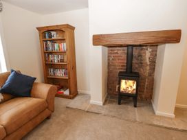 A living room with a brown sofa, wooden bookshelf filled with books, and a wood-burning stove in a brick fireplace at The Groom's Cottage in Goodmanham Wold near Market Weighton
