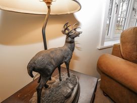 A deer sculpture on a wooden table next to a lamp and a brown armchair near a window at The Groom's Cottage in Goodmanham Wold near Market Weighton