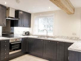 A kitchen with dark cabinets white marble countertops a built-in oven electric stove a stainless steel sink and a window with blinds at The Groom's Cottage