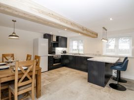 A kitchen with black cabinets, marble countertops, wooden dining table with chairs, and two blue bar stools at The Groom's Cottage in Goodmanham Wold near Market Weighton
