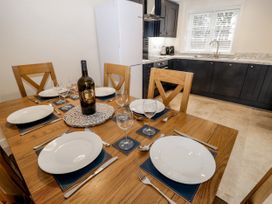 A dining table set with plates glasses and cutlery next to a kitchen with countertop cabinets and a window at The Groom's Cottage Goodmanham Wold near Market Weighton
