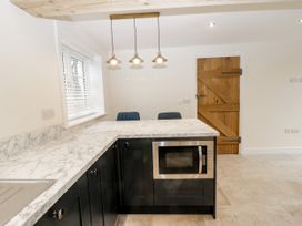 A kitchen with black cabinets a marble countertop a built-in microwave wooden door and three hanging lights at The Groom's Cottage Goodmanham Wold near Market Weighton