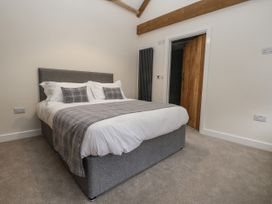 A bedroom with a grey upholstered bed and plaid bedding next to a wooden door and exposed wooden ceiling beams at The Groom's Cottage in Goodmanham Wold near Market Weighton