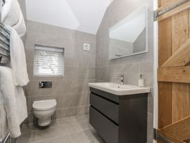 A bathroom with a wall-mounted toilet a sink with a black vanity and a rectangular mirror at The Groom's Cottage in Goodmanham Wold near Market Weighton