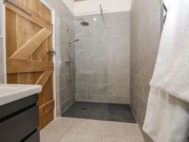 A tiled shower area with a glass screen wooden door and towels hanging at The Groom's Cottage in Goodmanham Wold near Market Weighton