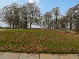 An outdoor area with grass and fallen leaves surrounded by a wooden fence and leafless trees at The Groom's Cottage in Goodmanham Wold near Market Weighton