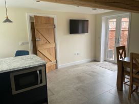 A kitchen with a wooden door a wall-mounted television a marble countertop with a microwave under it and glass double doors leading outside at The Groom's Cottage in Goodmanham Wold near Market Weighton