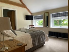 A bedroom with a bed, wooden nightstand with a lamp, a wall-mounted TV, two windows with plaid blinds, a chair, and a wall mirror at The Groom's Cottage Goodmanham Wold near Market Weighton