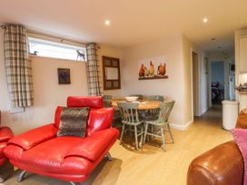 A dining area with a round wooden table and green chairs next to a living room with red leather chairs at The Old Hen Shed in Hainworth near Haworth
