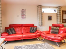 A living room with red leather sofas and plaid curtains at The Old Hen Shed in Hainworth near Haworth