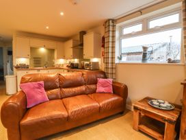 A kitchen and sitting area with a brown leather sofa with two pink cushions and a wooden side table with crockery at The Old Hen Shed in Hainworth near Haworth