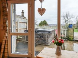 A wooden table with a vase of flowers inside looking through glass doors to a patio with a hot tub and a chair at The Old Hen Shed in Hainworth near Haworth