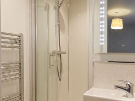 A bathroom with a shower enclosure a towel radiator a sink with a faucet and a lighted mirror at The Old Hen Shed in Hainworth near Haworth