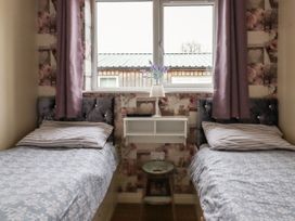 A bedroom with two single beds a window in the middle and a small shelf with a lamp at The Old Hen Shed in Hainworth near Haworth