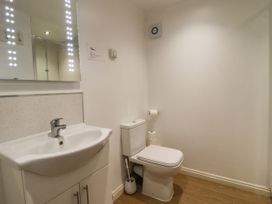 A bathroom with a white sink and a toilet with toilet paper and a brush on a wooden floor at The Old Hen Shed in Hainworth near Haworth