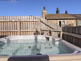 An outdoor hot tub with water and a bottle of wine with two glasses on the edge surrounded by wooden fencing at The Old Hen Shed in Hainworth near Haworth