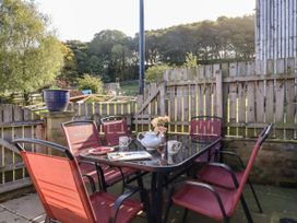 An outdoor patio with a glass table and six red chairs surrounded by a wooden fence at The Old Hen Shed in Hainworth near Haworth