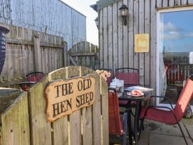 An outdoor patio with a wooden gate and a sign reading The Old Hen Shed with red chairs around a black table at The Old Hen Shed in Hainworth near Haworth