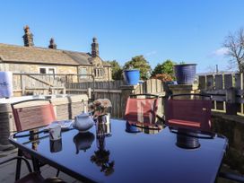 An outdoor patio with a glass table and red chairs near a hot tub and a stone house at The Old Hen Shed in Hainworth near Haworth