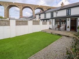 A backyard with green lawn stone patio with chairs white house and stone arch bridge in the background at Anneth Lowen in Angarrack near Hayle