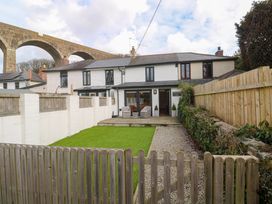 A fenced backyard with a lawn dining chairs and stone path behind a terraced house with a viaduct in the background at Anneth Lowen in Angarrack near Hayle