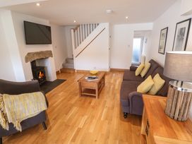 A living room with a wood burning stove a mounted TV a brown sofa with yellow cushions a wooden coffee table and a wooden sideboard with a lamp at Anneth Lowen in Angarrack near Hayle