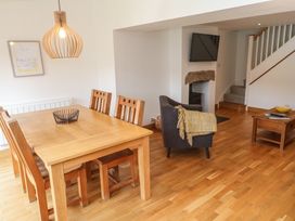 A dining area with a wooden table and chairs next to a sitting area with an armchair and a wall-mounted TV at Anneth Lowen Angarrack near Hayle
