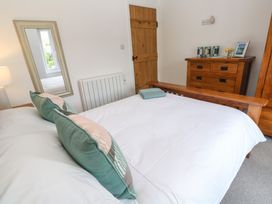 A bedroom with a white bed and green pillows a wooden dresser a wooden door and a mirror at Anneth Lowen Angarrack near Hayle